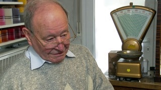 Der 87-jährige Heinz Rittberger steht in seinem Seifenladen in Stuttgart. Neben ihm steht eine Waage.