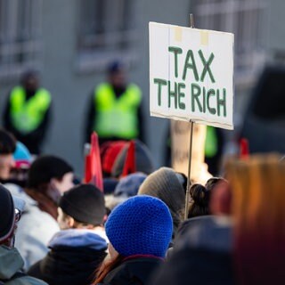 Auf einem Schild steht bei einer Demonstration steht "tax the rich". In einem offenen Brief fordern Superreiche für höhere Steuern für sich.