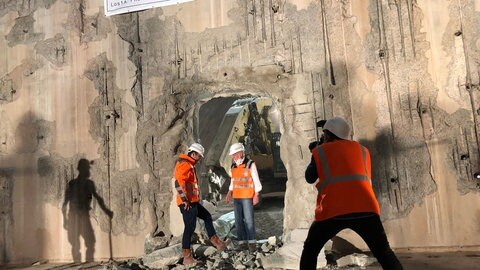Mehrere Bauarbeiter in einem Tunnel, in den ein Bagger ein Loch geschlagen hat,
