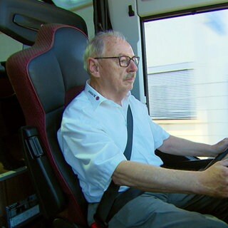 Georg Nußbaum trägt ein weißes Hemd und sitzt am Lenkrad eines Reisebusses. Er schaut nach rechts.