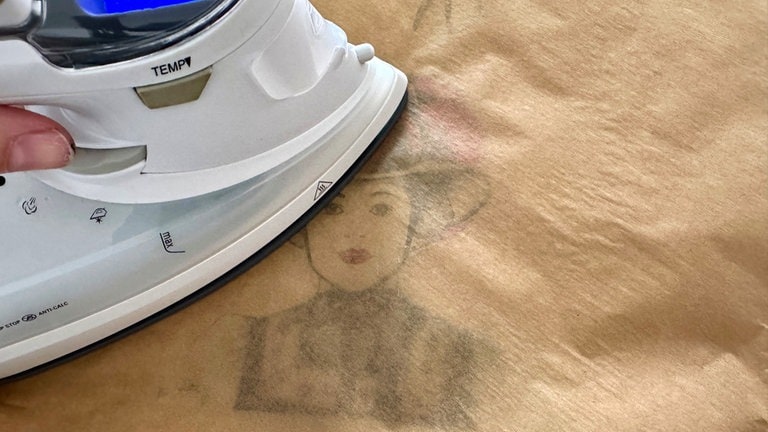 Auf die Tasche, oder was auch immer der gewählte Stoff ist, drauflegen. Ein Stück Backpapier darüber legen und auf heißer Stufe ca. 1 Minute bügeln. 