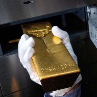 (Symbolbild) Eine Hand schiebt einen Goldbarren in ein Tresor. Unbekannte stehlen in Bruchsal Gold im Millionenwert. Sie hatten sich vorher als falsche Polizisten ausgegeben.