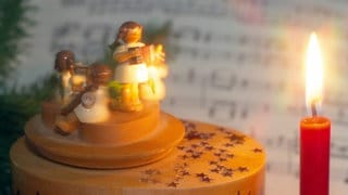 Symboldbild Weihnachtslieder: Weihnachtsspieluhr neben einer brennenden Weihnachtskerze