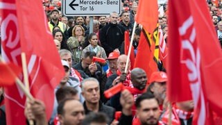 Mitarbeitende der Mercedes-Benz AG stehen während einer Aktion der IG Metall auf einer Zufahrt zum Mercedes-Benz Werk.