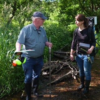 Gewässerökologe Dr. Hans-Jürgen Hahn und Dr. Heide Stein stehen im Guldenbach mit einem Messgerät.