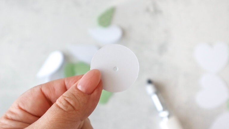 Bevor die gefalteten Herzen auf den Papierkreis geklebt werden, ein Loch in die Mitte des Kreises stechen. Das geht super mit einem Schaschlikspieß oder einem Lochstanzer. 