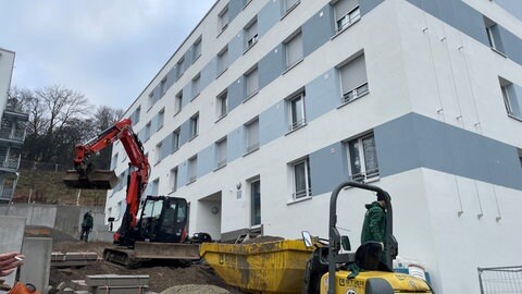 Ein Container und ein Bagger vor den fast fertigen neuen Personalwohnungen der Uniklinik Tübingen