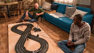 Heinz und Tayo sitzen auf dem Boden und spielen mit der Rennbahn