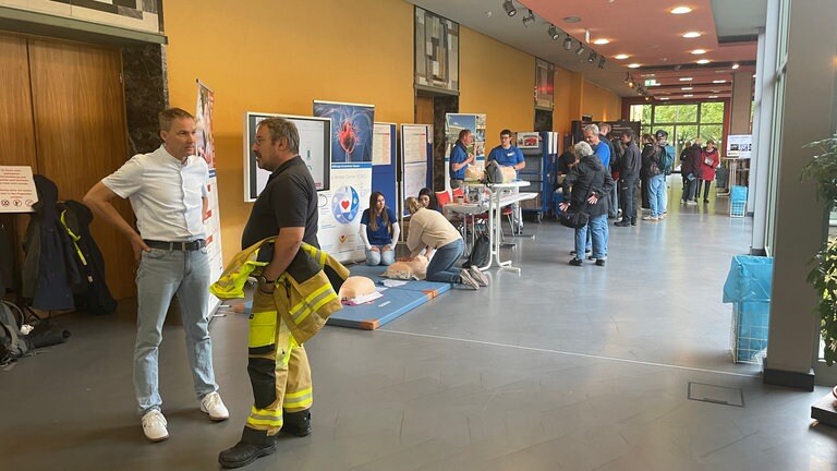 Der erste Bevölkerungsschutztag in Speyer: So sah es in der Stadthalle am Freitagmorgen aus. Es laufen Menschen durch die Stadthalle, es sind Infostände zu sehen und eine Frau, die an einer Puppe übt, wie man jemanden reanimiert.