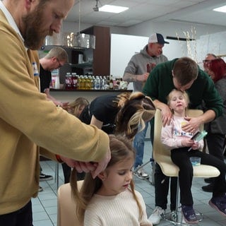 In einem Friseursalon in Bad Kreuznach wird Männern erklärt, wie man mit langen Haaren umgeht und sie frisiert.