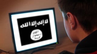 Jugendlicher sitzt am Bildschirm eines PC s mit Flagge des IS Islamischer Staat.