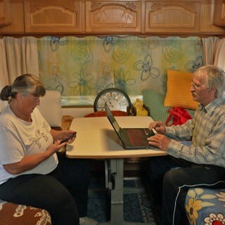Anka (l.) und Thomas Blödorn arbeiten am Handy und am Laptop in ihrem Wohnwagen