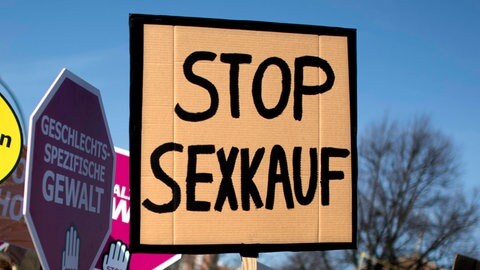 Bei einer Demo wird ein Schild mit der Aufschrift "Stop Sexkauf" hochgehalten.