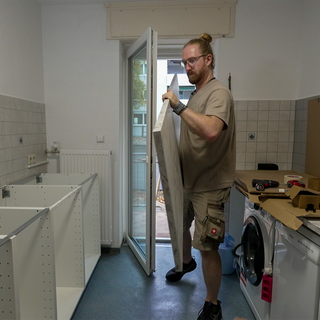Ein Mann trägt eine Arbeitsplatte in einen Raum, in dem eine Küche aufgebaut wird. 