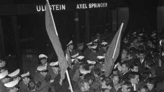Demonstranten mit roten Fahnen vor dem Springer-Hochhaus in der Kochstraße. Eine Welle von Protestdemonstrationen hat das Attentat auf den Berliner SDS-Ideologen Rudi Dutschke ausgelöst. Dutschke wurde am 11. April 1968 in Berlin vor der Geschäftsstelle des Sozialistischen Deutschen Studentenbundes (SDS) am Kurfürstendamm von Josef Erwin Bachmann niedergeschossen und lebensgefährlich verletzt. Die Demonstrationen richteten sich hauptsächlich gegen Gebäude des Axel-Springer-Verlages, der vom SDS als "Zentrum der systematischen Hetzkampagne gegen politische Minderheiten" bezeichnet wird. 