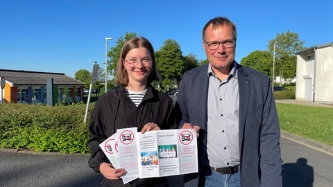 Schülersprecherin Emma Lucke und Schulleiter Dirk Weigand zeigen den Flyer, in dem mehrere alternative Parkplätze in der Nähe des Schulzentrums für die Eltern markiert sind. 