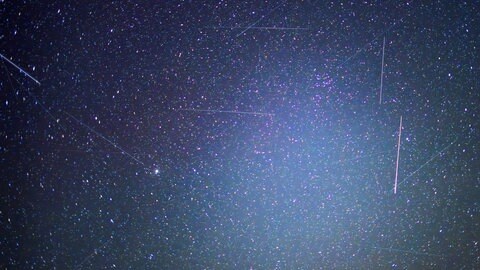 Satelliten und andere Objekte sind als Leuchtspuren zwischen den Sternen am Nachthimmel zu sehen. Ob auch ein UFO dabei ist? Über 1.000 Mal meldeten sich 2024 Menschen bei der UFO-Meldestelle CENAP, weil sie ein unbekanntes Flugobjekt am Himmel entdeckt haben. Ein Außerirdischer war aber nicht dabei.