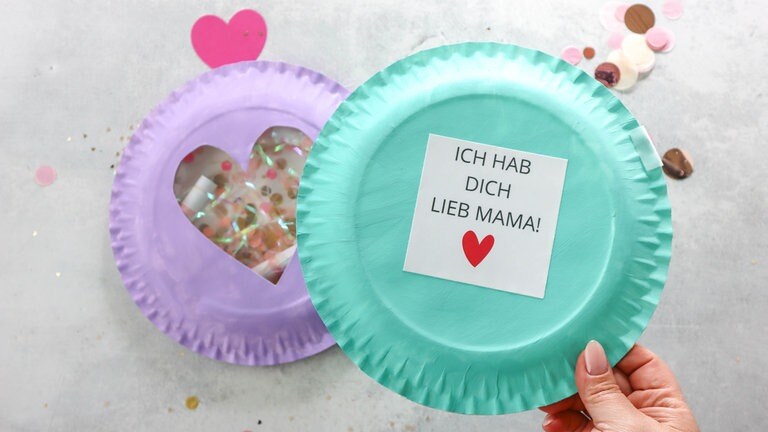 Den Pappteller mit Fenster auf den unteren legen und rundherum mit Heißkleber oder Bastelkleber zusammenkleben. 