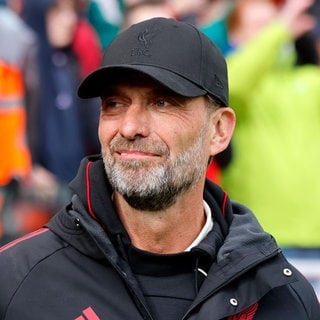Jürgen Klopp steht mit Trainingsjacke und Kappe an der Trainerbank. 