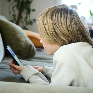 Ein Junge liegt auf einem Sofa und guckt auf sein Smartphone (Symboldbild). Die Tübinger Kinder- und Jugendpsychologin Isabel Brandhorst hat sich für ein Verbot von Social Media für Minderjährige ausgesprochen.