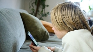 Ein Junge liegt auf einem Sofa und guckt auf sein Smartphone (Symboldbild). Die Tübinger Kinder- und Jugendpsychologin Isabel Brandhorst hat sich für ein Verbot von Social Media für Minderjährige ausgesprochen.