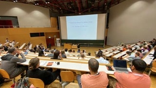 Im Hörsaal der Universität Konstanz sind zahlreiche Mathematiker. Sie hören einen Vortrag des renommierten Wissenschaftlers June E. Huh.