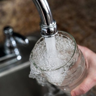 Symbolbild Wasserverseuchung mit PFAS: Wasser fließt aus einem Wasserhahn in ein Glas