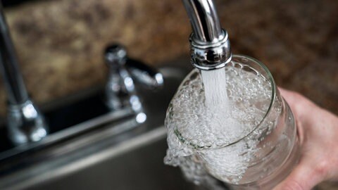 Symbolbild Wasserverseuchung mit PFAS: Wasser fließt aus einem Wasserhahn in ein Glas