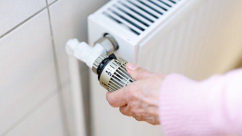 Eine Frau stellt an einem Thermostaten die Temperatur von einem Heizkörper ein.