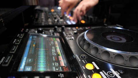 Ein DJ steht an Turntables.