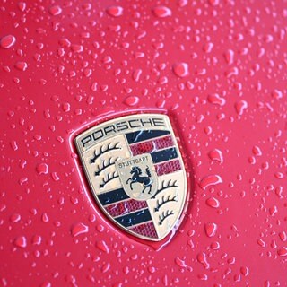 Regentropfen auf einem roten Auto mit Porsche-Logo. Der Autobauer verkauft im ersten Halbjahr 2025 weniger Autos. (Symbolbild)