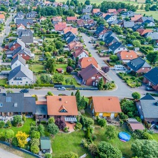 Häuser in direkter Nachbarschaft zueinander. Bäume und Hecken säumen die Grundstücksgrenzen.
