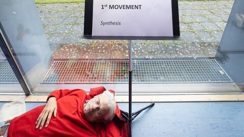 Mann liegt mit geschlossenen Augen am Fuße eines Notenständers
