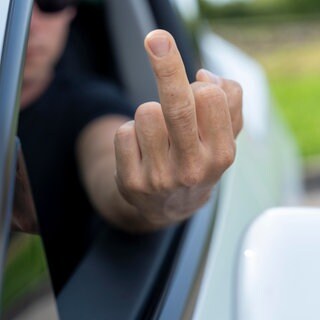 Wütender Autofahrer zeigt einen Mittelfinger als Beleidigung im Straßenverkehr.