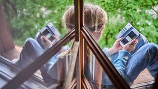 Ein Kind sitzt am Fenster und schaut auf sein Handy