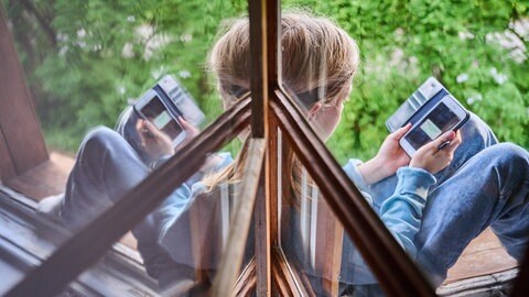 Ein Kind sitzt am Fenster und schaut auf sein Handy