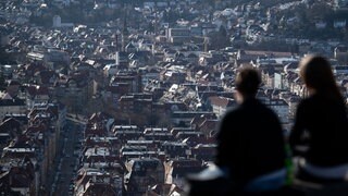 Zwei junge Frauen sitzen am Rande einer Aussichtsplattform mit Blick über Stuttgart in der Sonne: In Stuttgart führt die Reform der Grundsteuer zu Ärger. Ein Grund dafür sind die sogenannten Bodenrichtwert-Zonen.