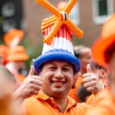 Ein Fan der niederländischen Nationalmannschaft in Orange gekleidet mit einer Kopfbedeckung in Mühlenform. Warum ist Orange eine Art Nationalfarbe der Niederlande? Die einfache Antwort findet man im Namen des Königshauses, denn die niederländischen Könige stammen aus dem Adelshaus Oranien-Nassau.