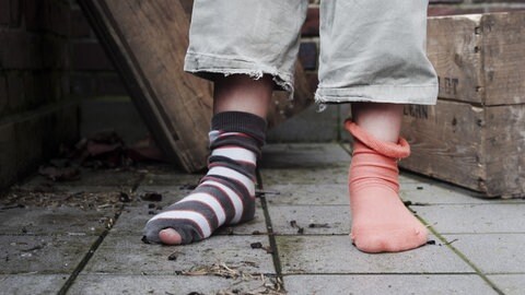 Kinderarmut: ein Kind mit zwei unterschiedlichen Socken, ein geringelter Strumpf ist kaputt.