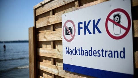 Symbolbild: Das FKK-Schild weist auf den Nacktbadestrand hinter dem Sichtschutz hin