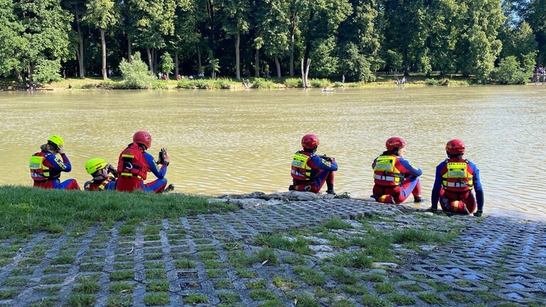 Mehrere Einsatzkräfte der DLRG sitzen am Donauufer und warten auf die Nabader.