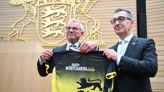 Der neu gewählte Ministerpräsident Cem Özdemir bekommt von Thomas Strobl ein Trikot mit dem Logo des Landes Baden-Württemberg.