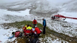 Rettungskräfte kümmern sich um den verletzten Wanderer aus Ettlingen. Er hat die Nacht im Schnee verbracht. Daneben steht ein Rettungshubschrauber. 