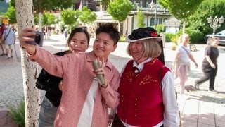 Zwei Touristen aus China machen ein Foto mit einer Fremdenführerein die das Kostüm einer Magd vom Bierhus trägt.