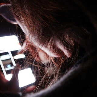 Eine junge Frau bedient ihr Smartphone im Dunkeln.