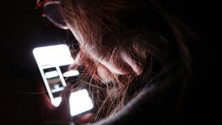 Eine junge Frau bedient ihr Smartphone im Dunkeln.