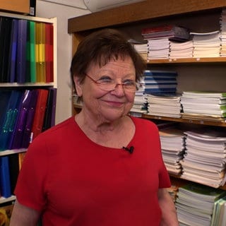 Inge Walter steht in ihrem Schreibwarengeschäft in Sinzheim vor Regalen mit Heften und Mappen. Sie trägt ein totes T-Shirt und eine Brille.