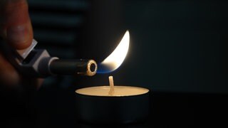 Eine Kerze wird mit einem Feuerzeug angezündet - für den Fall eines Blackouts sollten in jedem Haushalt Kerzen und Streichhölzer vorhanden sein.