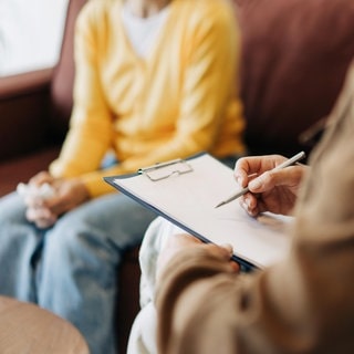 Therapeut macht in der Sitzung Notizen auf einem Klemmbrett: Spannungen im Therapieprozess gelten oft als Scheitern, dabei stellen sie oft den entscheidenden Wendepunkt dar. Aber wieso befördern Irritationen die Heilung? 