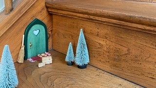 Trend für Weihnachten 2023: Wichteltür auf einer Treppe, kleine Bäume und Geschenke davor